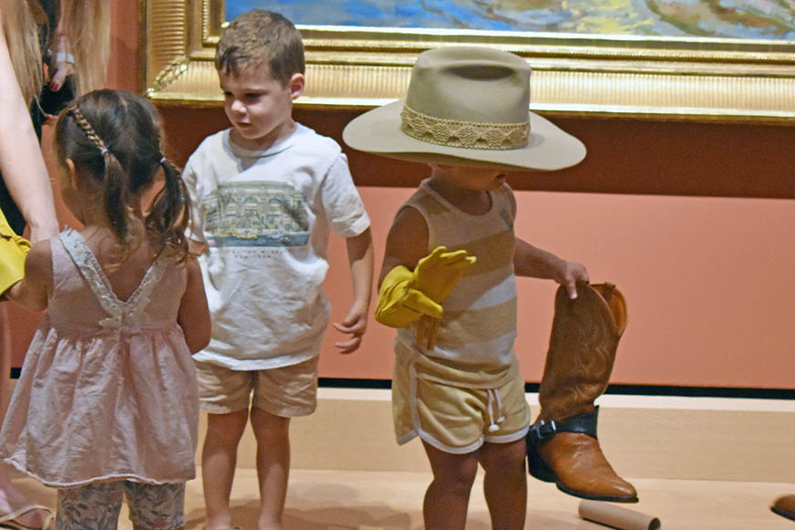 Little kid in a cowboy hat holding a boot