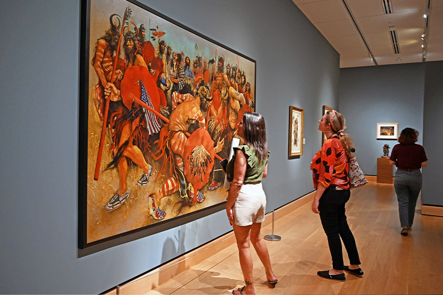 Visitors observing large, vibrant historical painting in gallery.