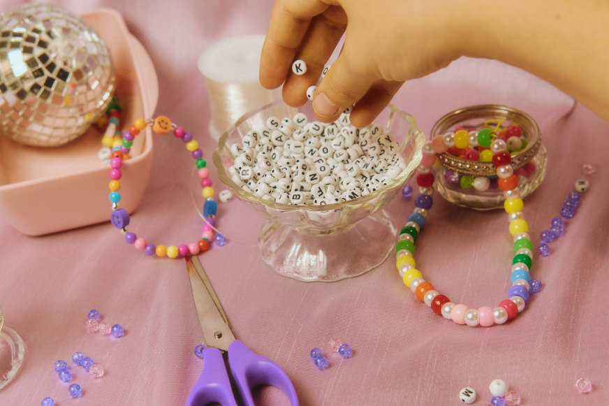 Hand crafting colorful beaded bracelets on table.