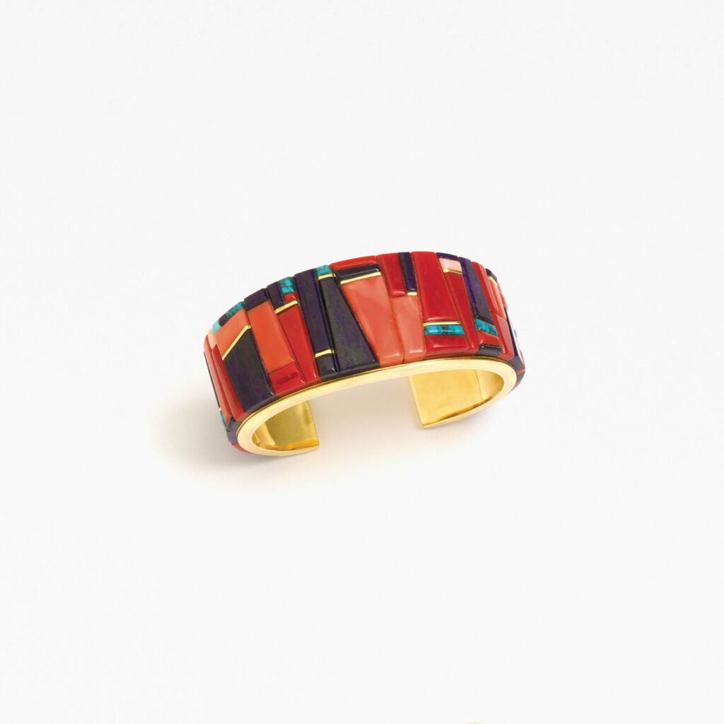A wide gold cuff bracelet from the Jewel Box collection, featuring inlaid rectangular pieces of red, purple, blue, and green stones arranged in a striking geometric pattern.