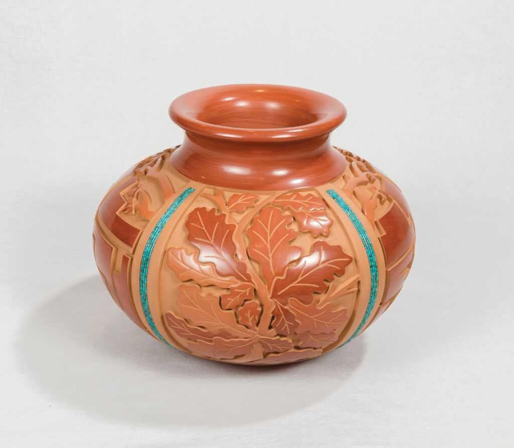 Round, terracotta-colored ceramic vase with carved leaf patterns and turquoise inlay accents, inspired by Native Art, set against a plain white background.