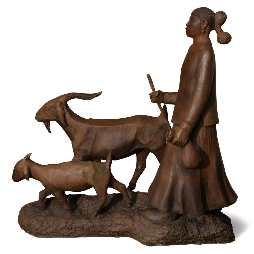 A wooden sculpture of a woman holding a stick and leading two goats, one large and one small, stands on a textured base—a striking example of Native Art perfect for any art gallery.