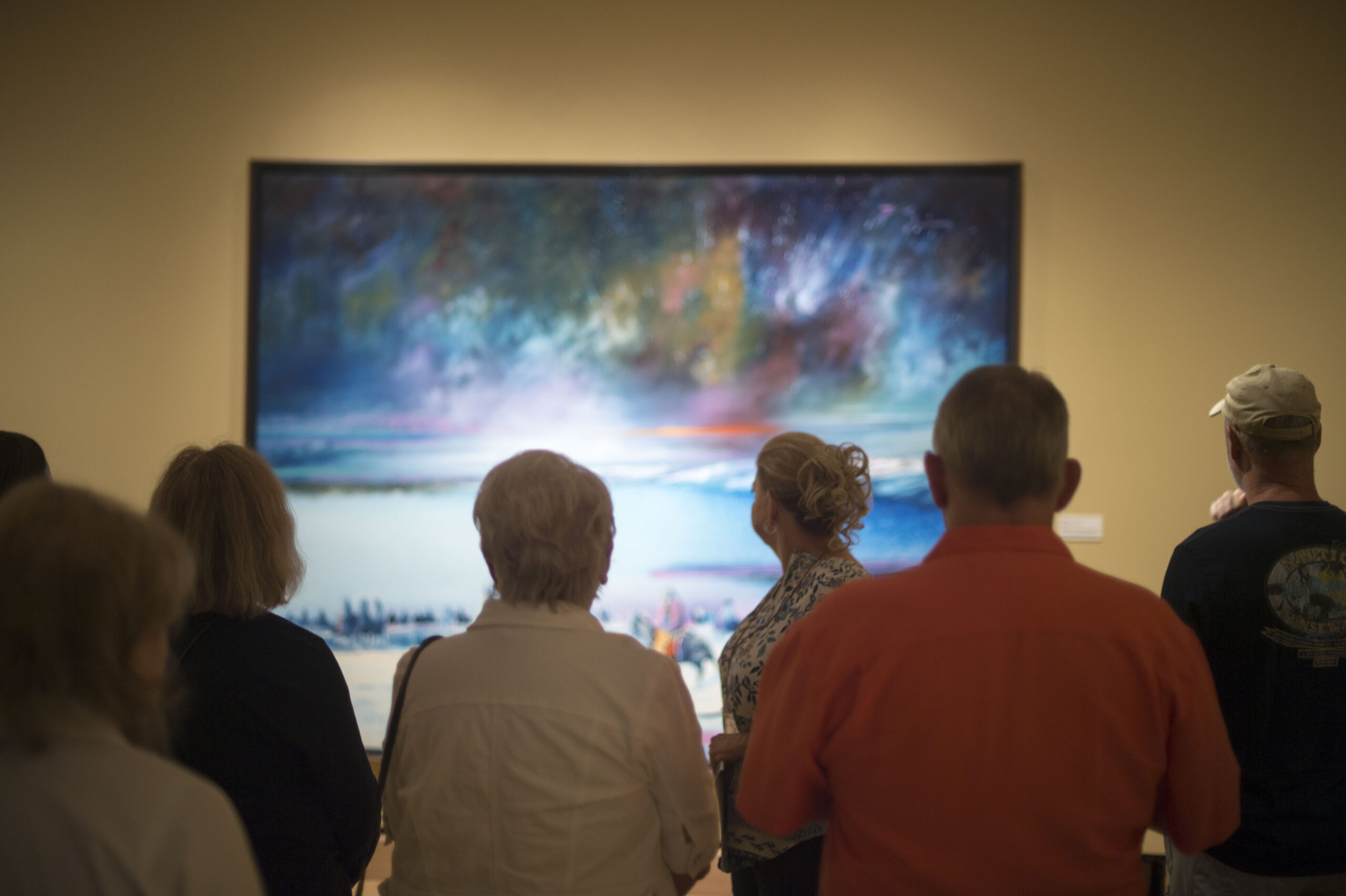 A group of people stands in front of a large, colorful abstract painting in an art gallery.