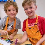 Two children painting with watercolors and smiling.
