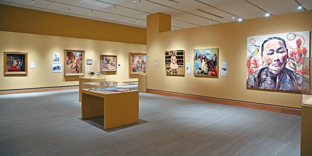 A modern art gallery with yellow walls displays various paintings and Chinese American exhibits in glass cases under bright ceiling lights.
