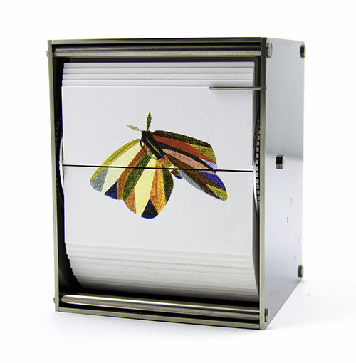 A metal flip card viewer displays a card with an illustration of a colorful moth, blending Wildlife themes with Contemporary Art in the Unnatural Selections series.