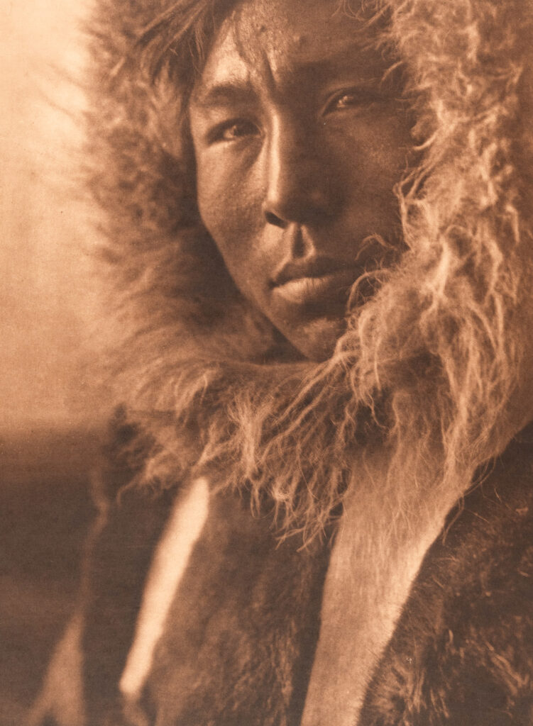 A person wearing a fur-lined hooded parka looks toward the camera with a neutral expression, reminiscent of a photograph by Edward S. Curtis. The image has a sepia tone.