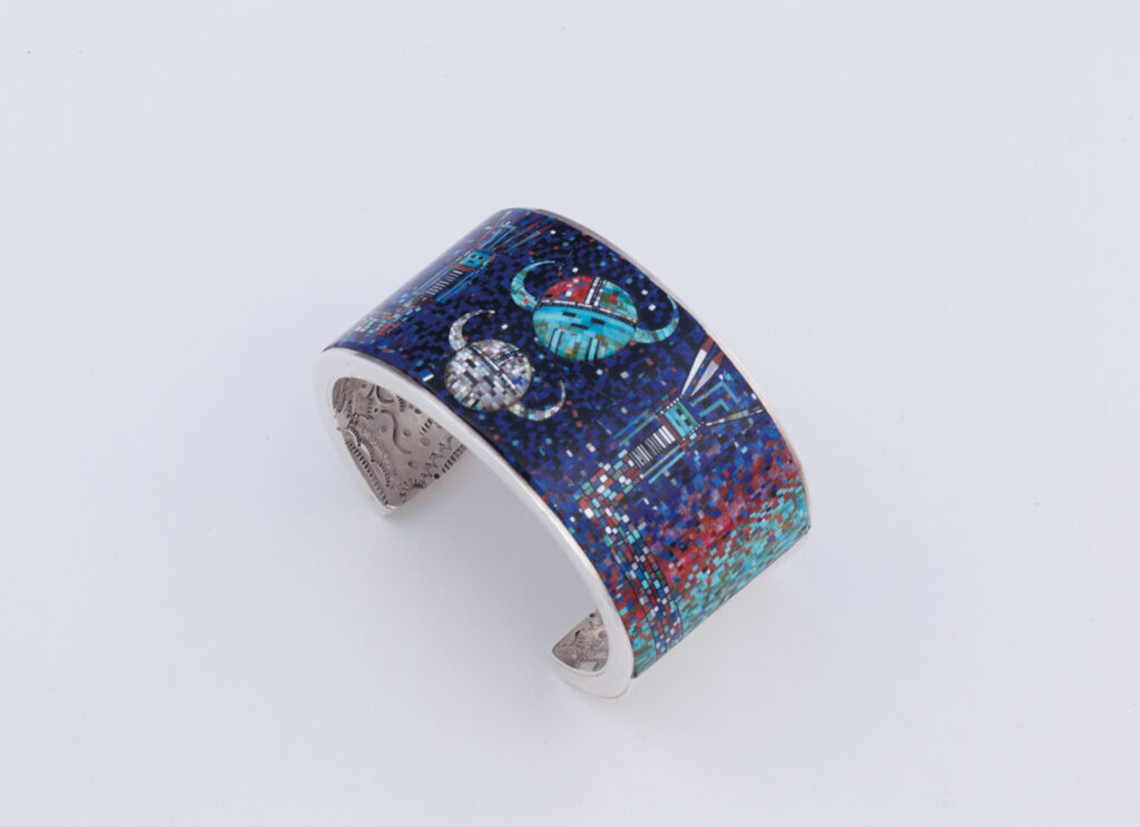 A wide silver cuff bracelet featuring a colorful, mosaic-style design with abstract shapes and patterns inspired by Western Art on a white background.