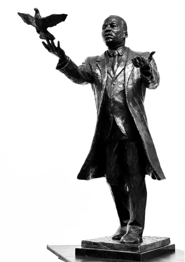 Bronze statue of a man in a suit reaching out with one hand toward a bird in flight, mounted on a rectangular base—symbolizing resilience and the enduring spirit captured by Black artists.
