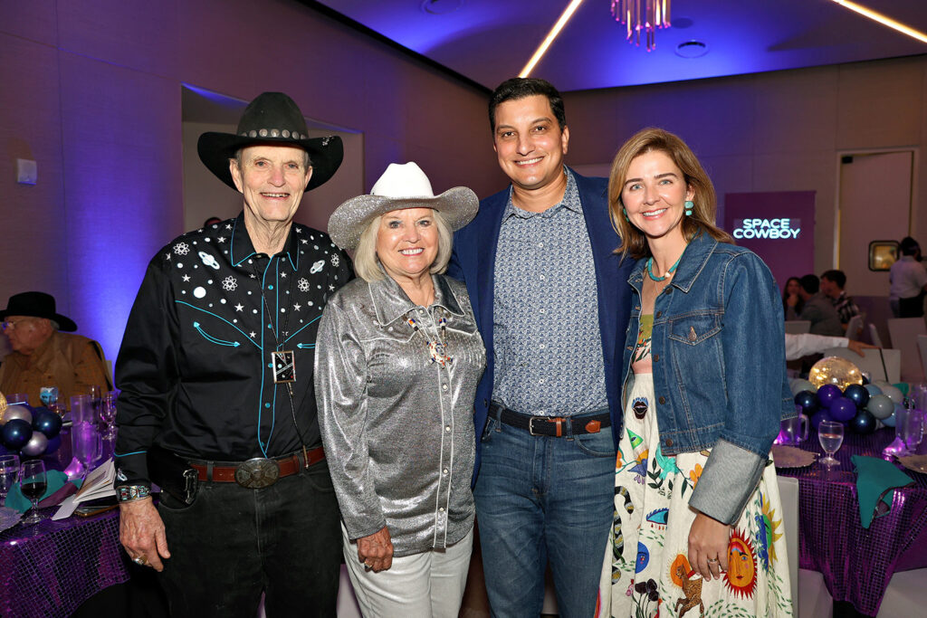 Four people pose together at an indoor Jamboree event with a "Space Cowboy" sign in the background; two are dressed in Western attire, two in business casual at The James.