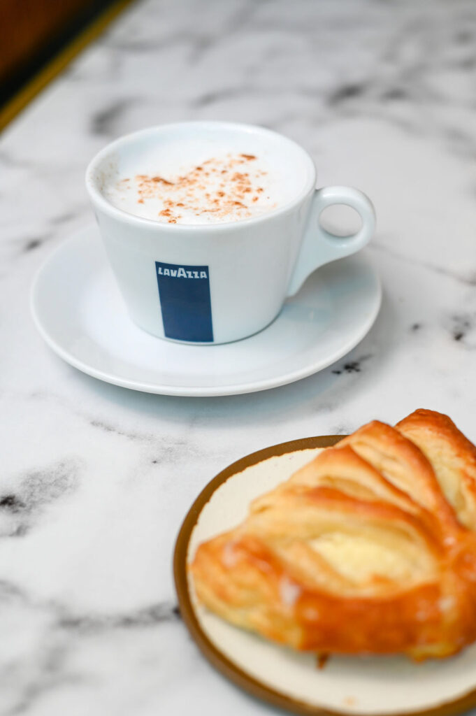 A lemon pastry with a cup of Lavazza cappuccino.