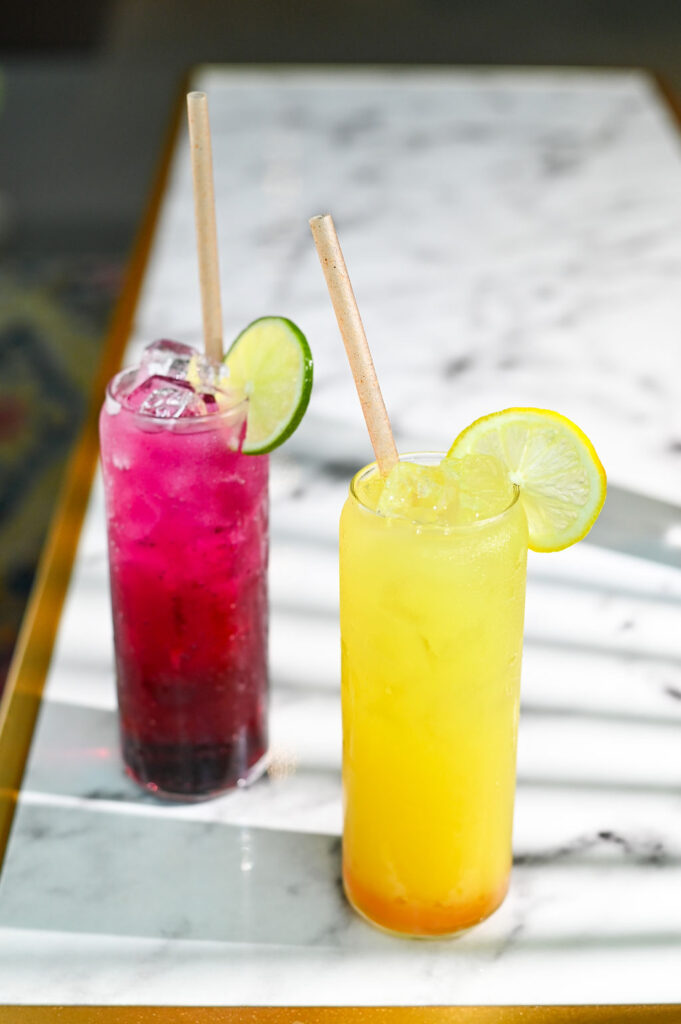 Two drinks, one pink and one yellow, garnished with a slice of citrus.