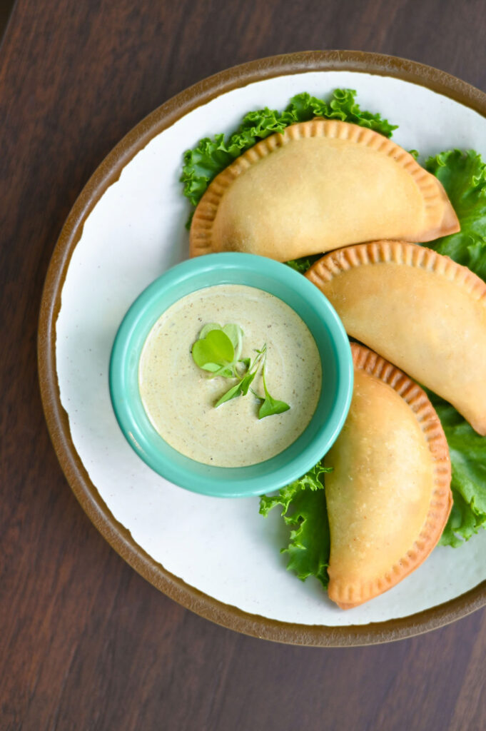 A plate of three empanadas with a dipping sauce.