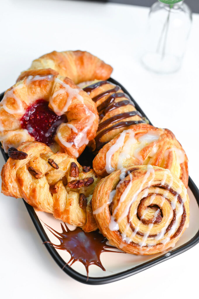 A plate of pastries including a cinnamon roll, croissant, and a raspberry Danish.
