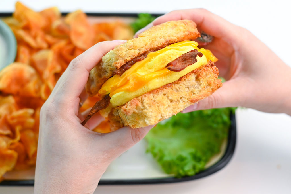 A hand holding the breakfast sandwich biscuit with eggs and bacon and cheese.