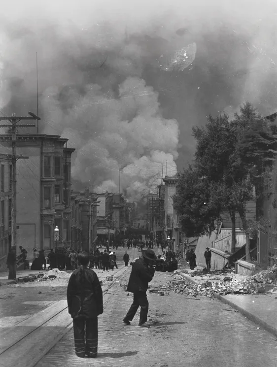 Black and white photo of people on a rubble-strewn city street, with smoke rising from buildings in the background after a major disaster, capturing the aftermath experienced in FarEast 06 Medicine emergency response.