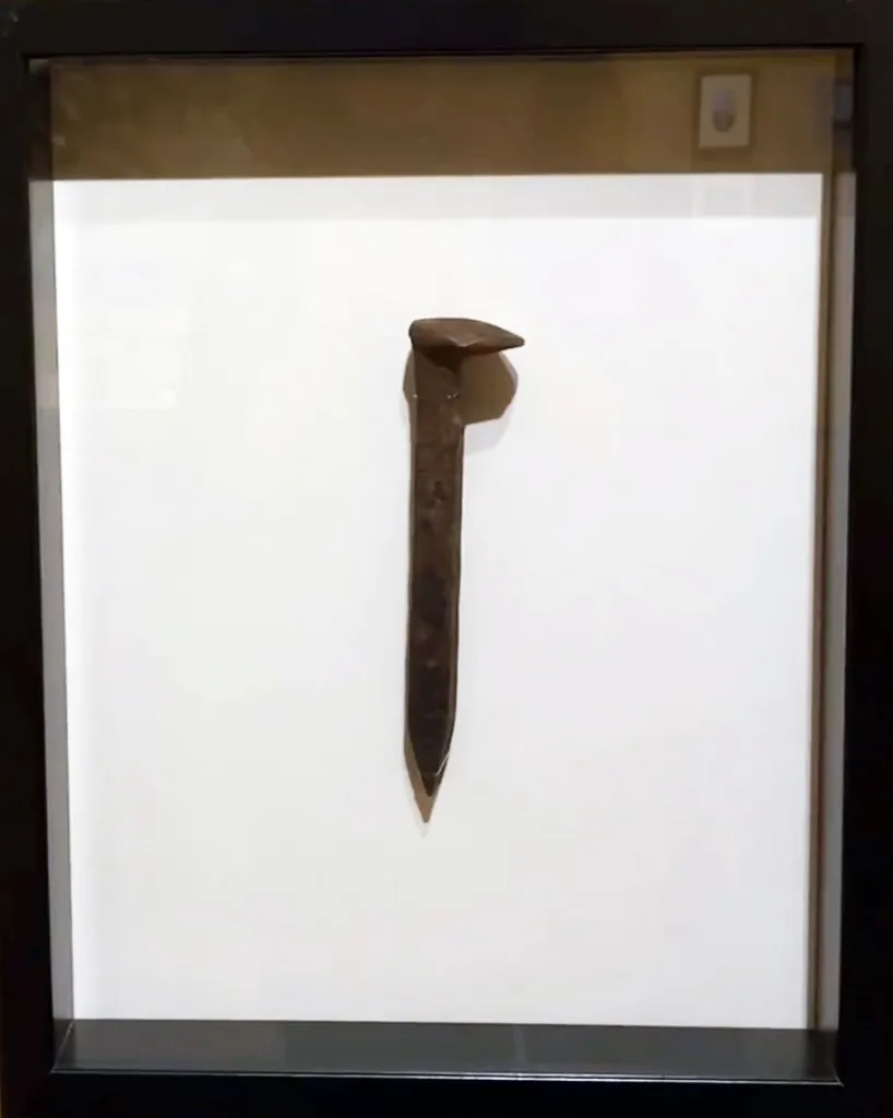 A single old FarEast 03 Railroad spike displayed vertically in a glass frame against a plain white background.