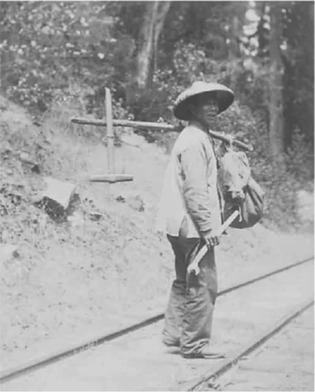 A worker wearing a broad-brimmed hat stands by railroad tracks near the Far East 02 Mining site, carrying tools and a bundle over his shoulder, with trees and a dirt embankment in the background.